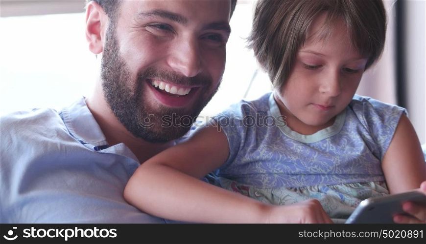 Father Daughter sitting in sofa playing games on tablet