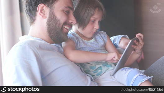 Father Daughter sitting in sofa playing games on tablet