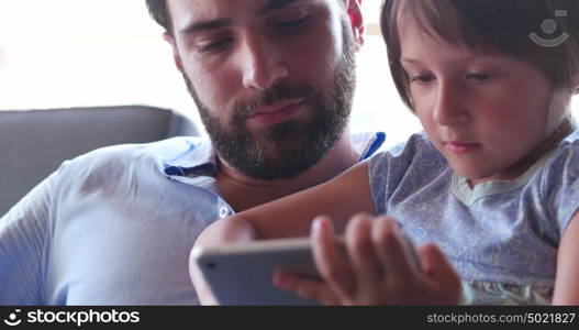 Father Daughter sitting in sofa playing games on tablet