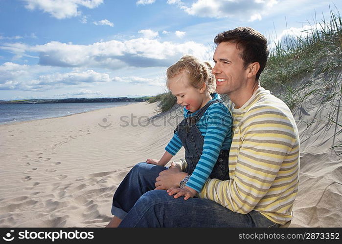 Father embracing daughter (5-6) sitting on beach