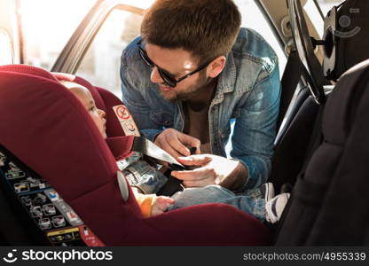 Father fasten his little baby in the car seat