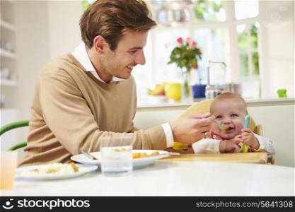 Father Feeding Baby Sitting In High Chair At Mealtime