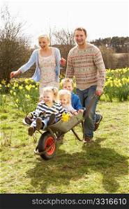 Father Giving Children Ride In Wheelbarrow Through Field Of Spring Daffodils