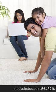 Father giving daughter a ride on his back with woman using laptop in the background