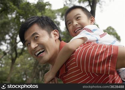 Father giving son piggyback (7-9) in park