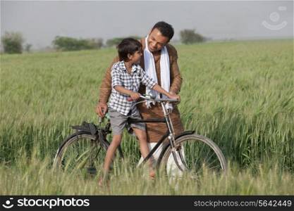 Father guiding son to ride cycle in the field