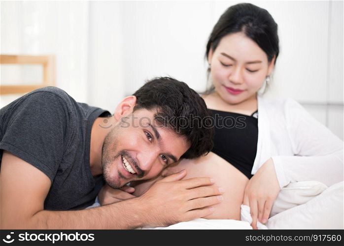 Father hearing his son or daughter kicking sound check inside mother belly when sitting on lying on bed at home. Family healthy and couples concept. Happy sweet home honeymoon and wedding theme