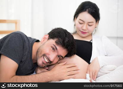 Father hearing his son or daughter kicking sound check inside mother belly when sitting on lying on bed at home. Family healthy and couples concept. Happy sweet home honeymoon and wedding theme