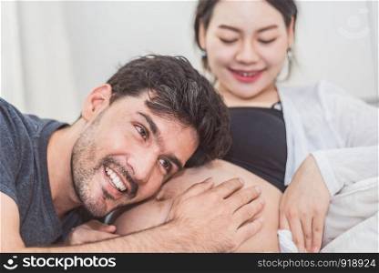 Father hearing his son or daughter kicking sound check inside mother belly when sitting on lying on bed at home. Family healthy and couples concept. Happy sweet home honeymoon and wedding theme