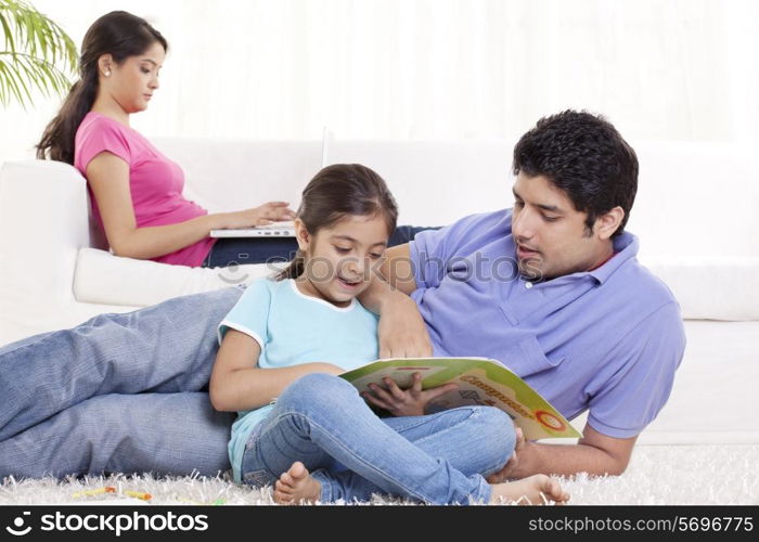 Father helping child in homework with woman using laptop in the background