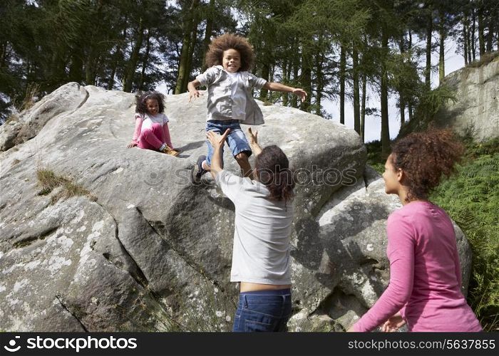 Father Helping Children To Jump Off Rocks