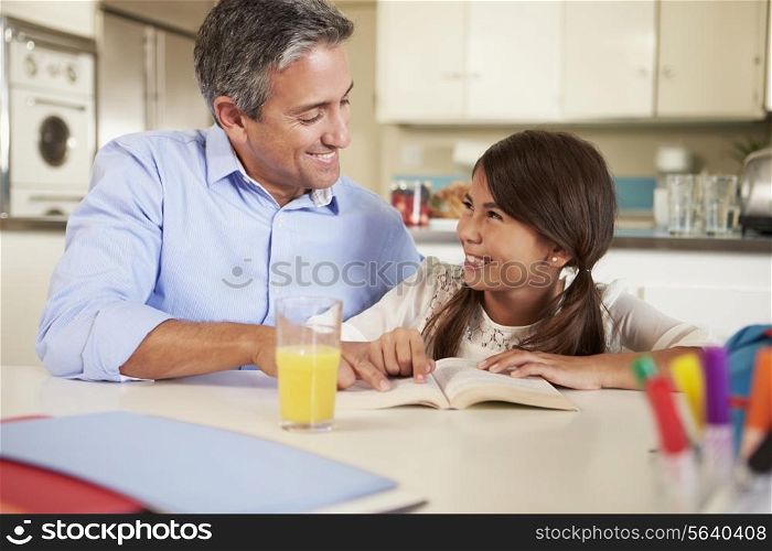 Father Helping Daughter With Reading Homework At Table