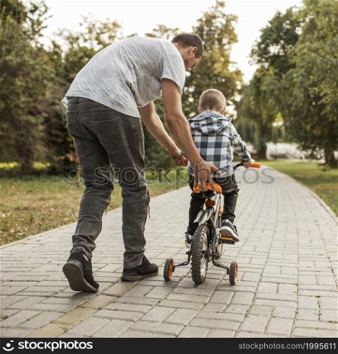 father helping his son riding bicycle from shot 1