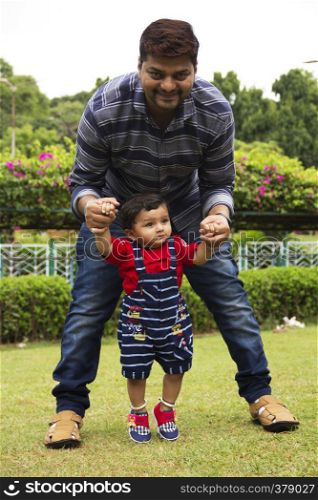 Father helping his toddler son to walk inside a garden, Pune, Maharashtra. Father helping his toddler son to walk inside a garden, Pune, Maharashtra.