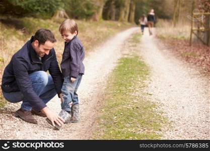 Father Helping Son To Put On Shoe During Family Walk