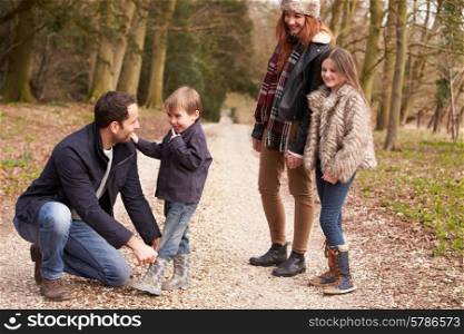 Father Helping Son To Put On Shoe During Family Walk