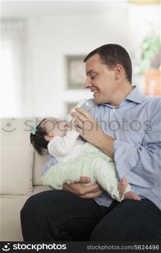 Father holding and feeding his baby daughter on the couch