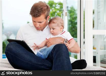 Father holding child while using digital tablet at home