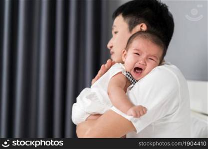 father holding crying baby on a bed