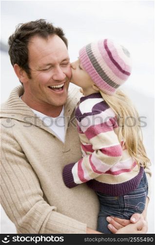 Father holding daughter kissing him at beach smiling