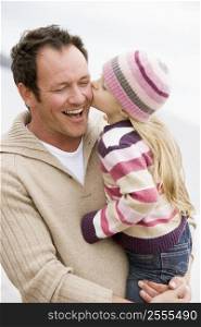 Father holding daughter kissing him at beach smiling