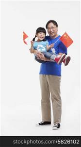 Father holding daughter, waving Chinese flags, studio shot