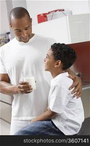 Father holding glass of milk, embracing son (7-9) indoors