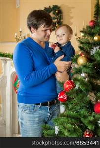 Father holding his baby son and looking at Christmas tree