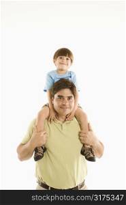 Father holding son on shoulders standing against white background.