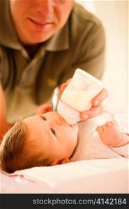 Father is feeding his baby with a bottle; very tranquil scene