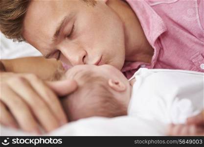 Father Kissing Baby Girl As They Lie In Bed Together