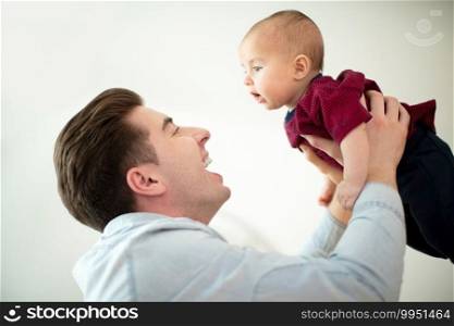 Father Lifting Smiling Baby Son Into Air At Home As They Play Game Together