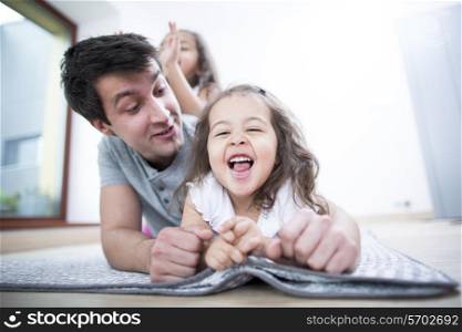 Father looking at cheerful daughter lying on blanket at home
