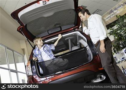 Father looking at son sitting in car trunk in showroom
