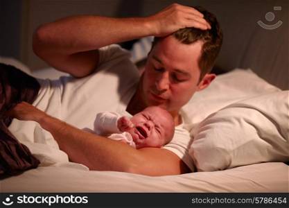 Father Lying In Bed With Crying Baby Daughter