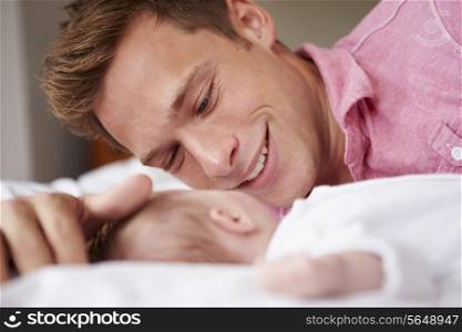 Father Playing With Baby Girl As They Lie In Bed Together