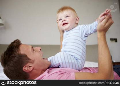 Father Playing With Baby Son As They Lie In Bed Together