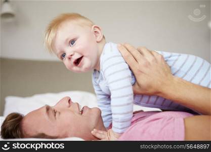 Father Playing With Baby Son As They Lie In Bed Together