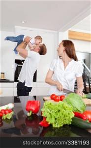 Father playing with child while mother cuts vegetables in kitchen