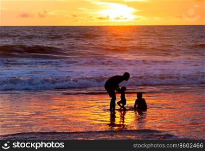 Father playing with children on beach by the oceanat at scenic sunset, Bali, Indonesia