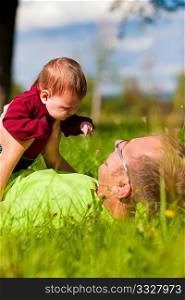 Father playing with his baby child on a great sunny day in a meadow with lots of green grass and wild flowers