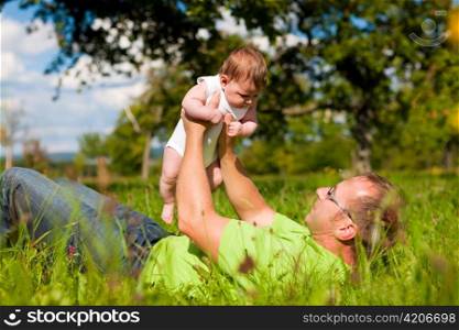 Father playing with his baby child on a great sunny day in a meadow with lots of green grass and wild flowers