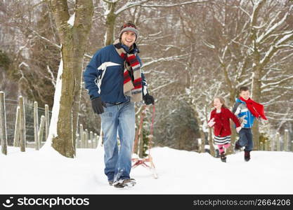 Father Pulling Children On Sledge Through Winter Landscape