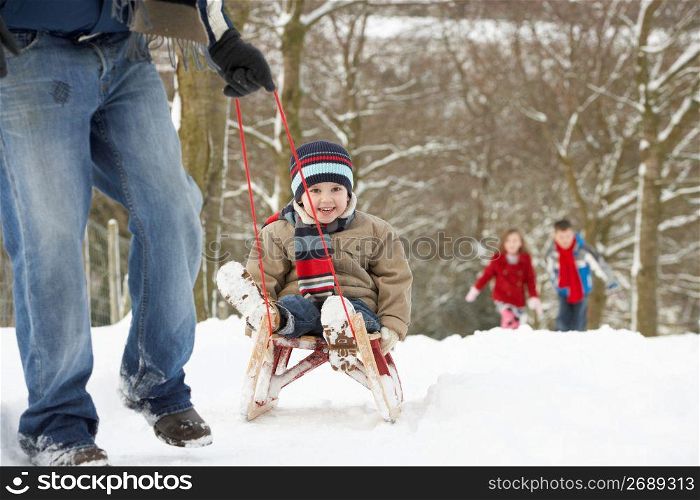 Father Pulling Children On Sledge Through Winter Landscape