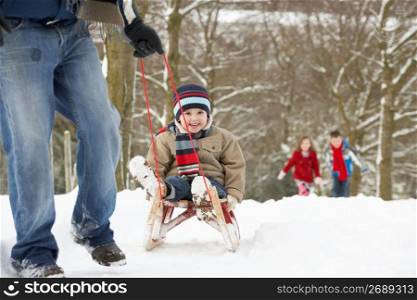 Father Pulling Children On Sledge Through Winter Landscape