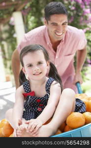 Father Pushing Daughter In Wheelbarrow Filled With Oranges