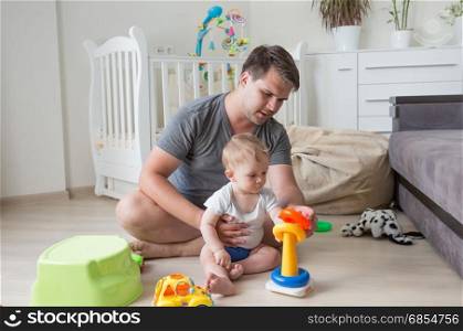 Father sitting on floor with his baby and playing with toys