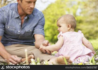 Father Sitting With Baby Girl In Field Of Summer Flowers
