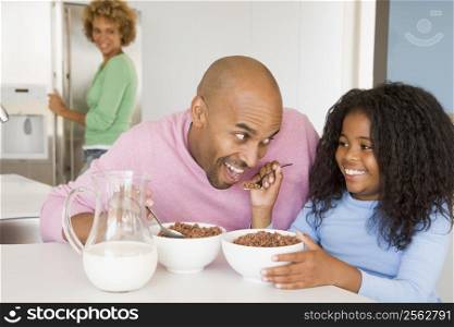 Father Sitting With Daughter As She They Eat Breakfast With Her Mother In The Background