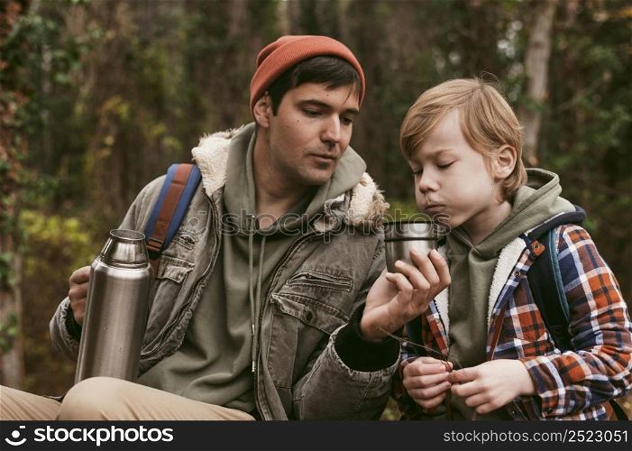 father son having hot tea outdoors nature
